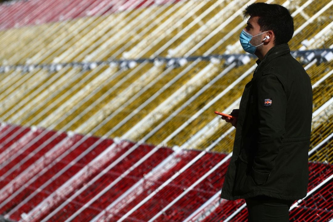 Un hombre con mascarilla pasa delante de la bandera de España con luces instalada en Madrid.