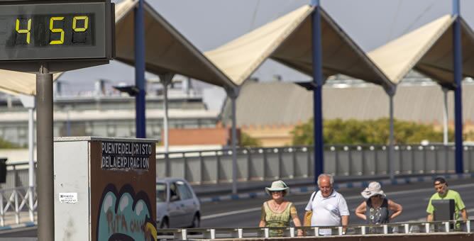 Unos turistas pasan junto a un termómetro que marca 45 grados en el Puente del Cristo de la Expiración en Sevilla