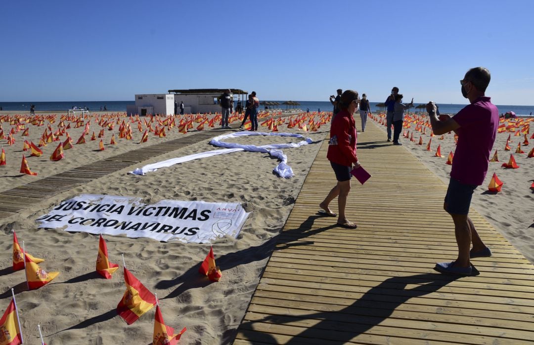 Varias personas visitan la Playa de la Patacona de Alboraia en la que se han colocado un total de 53.000 banderas de España en homenaje a los españoles fallecidos por coronavirus.