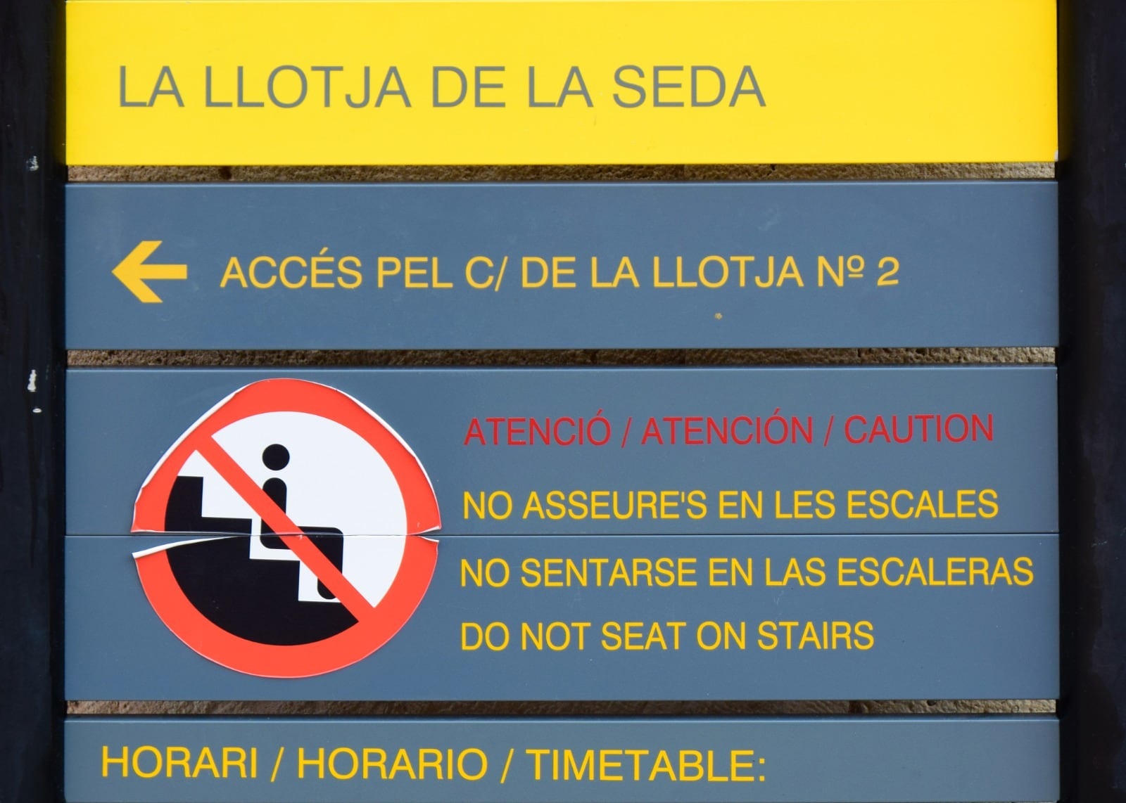 Panel que prohíbe sentarse en las escaleras de en la Lonja de la Seda.
