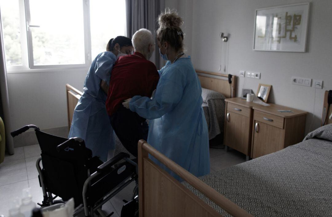 Una anciana es ayudada por dos trabajadoras en una residencia.