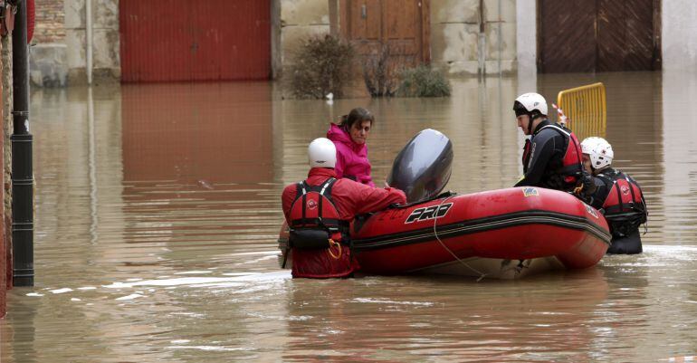 Voluntarios de Cruz Roja acompañan a una mujer hasta su casa por las calles anegadas del casco histórico de Tudela.