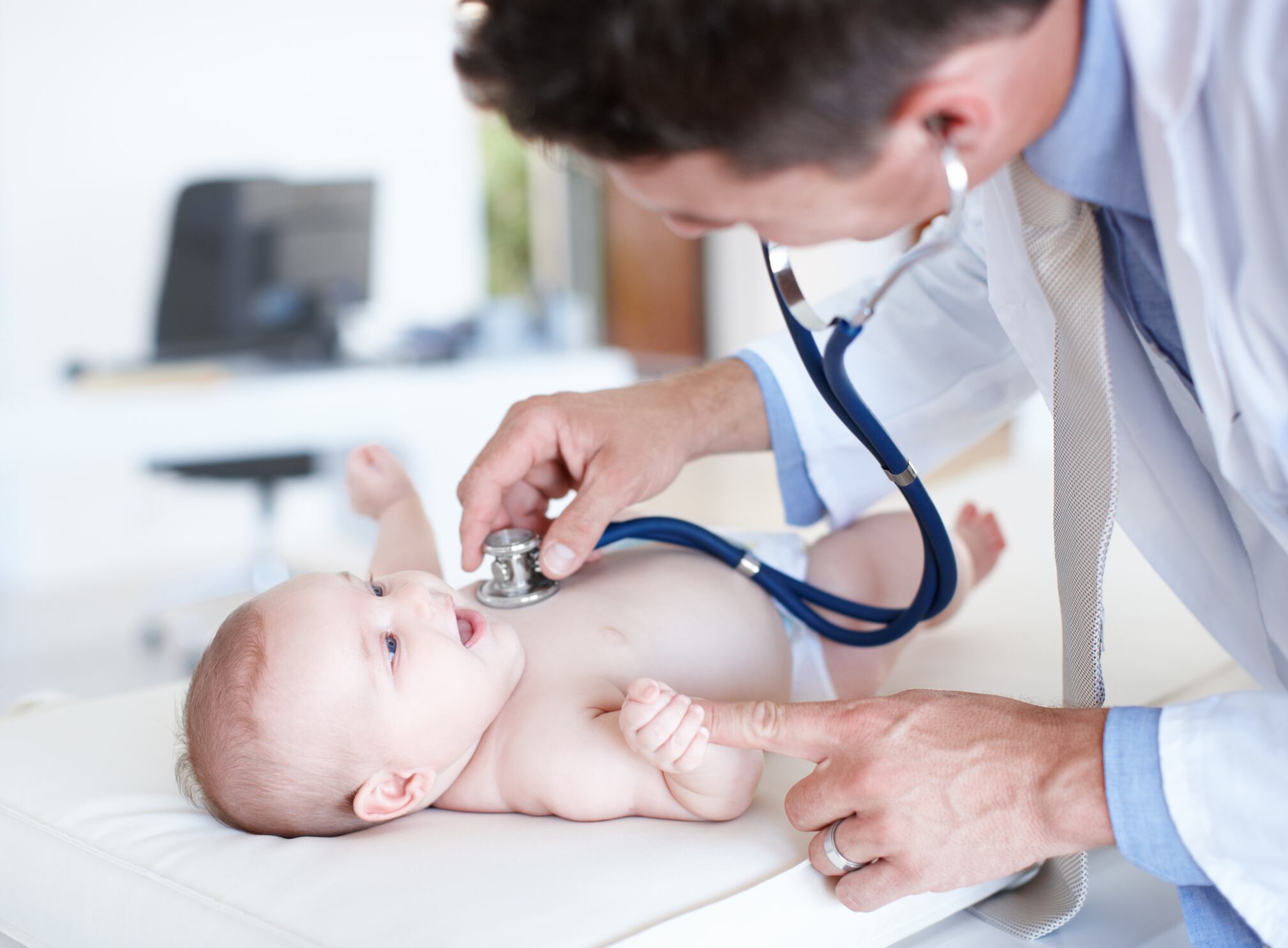 Delighted baby girl smiles at her pediatrician as he examines her chest with a stethoscope