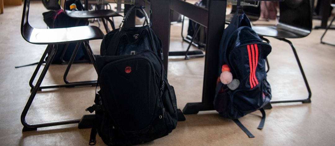 Mochilas colgadas en los pupitres de una clase