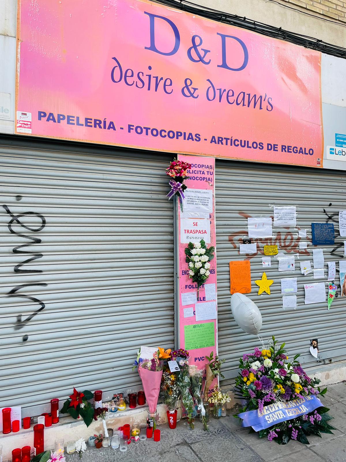 Flores, velas y mensajes de despedida a las puerta del comercio de Arturo Sánchez Ménendez en la calle San Vicente de Paul de Triana.