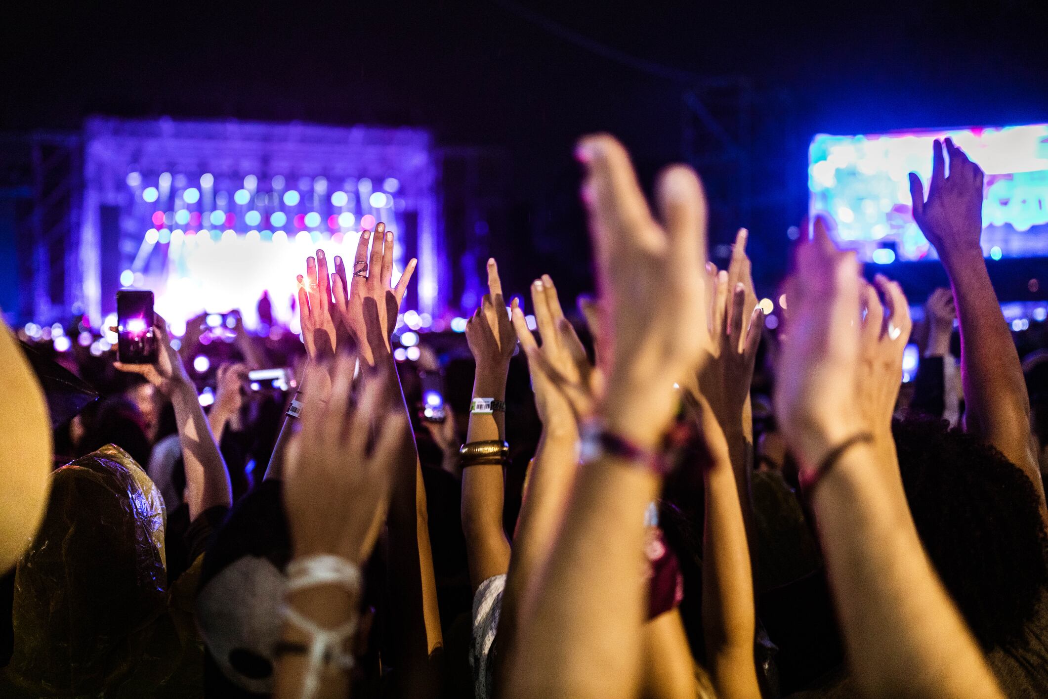 Público con las manos levantadas participando en un concierto en vivo frente a un escenario iluminado