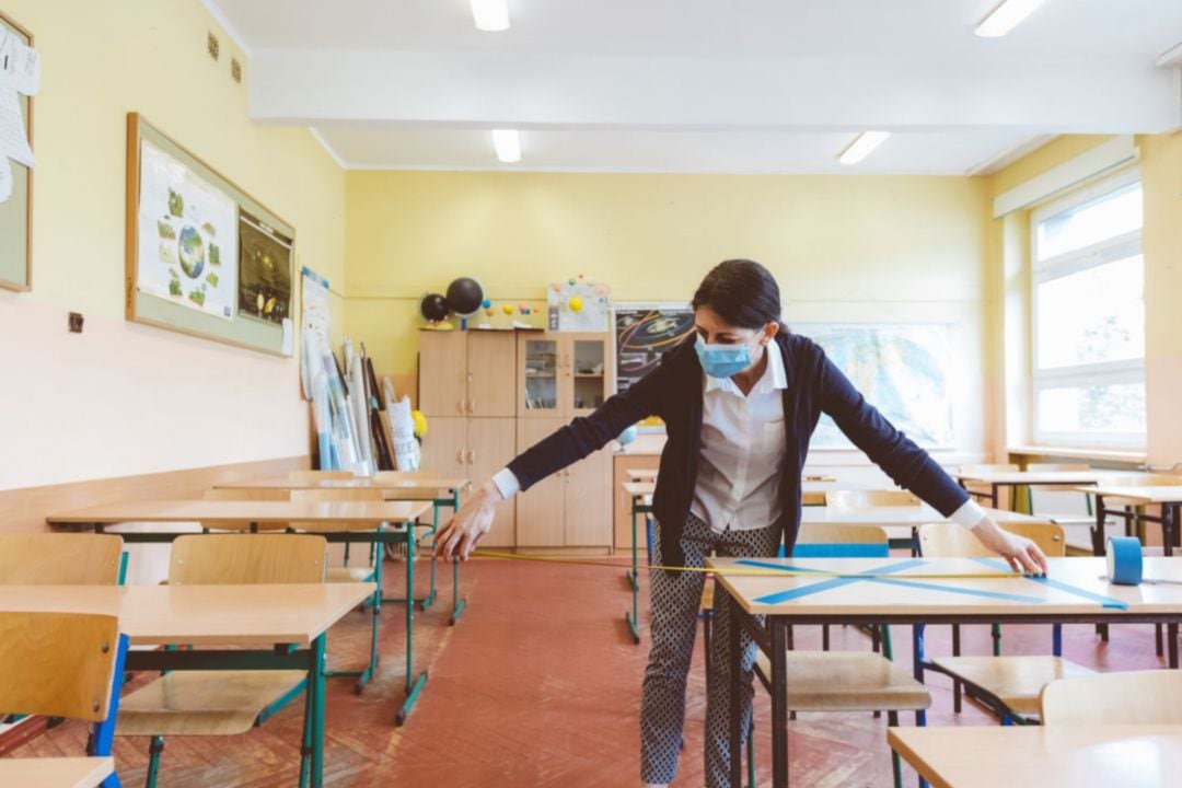 Una profesora toma medidas entre pupitres en un aula