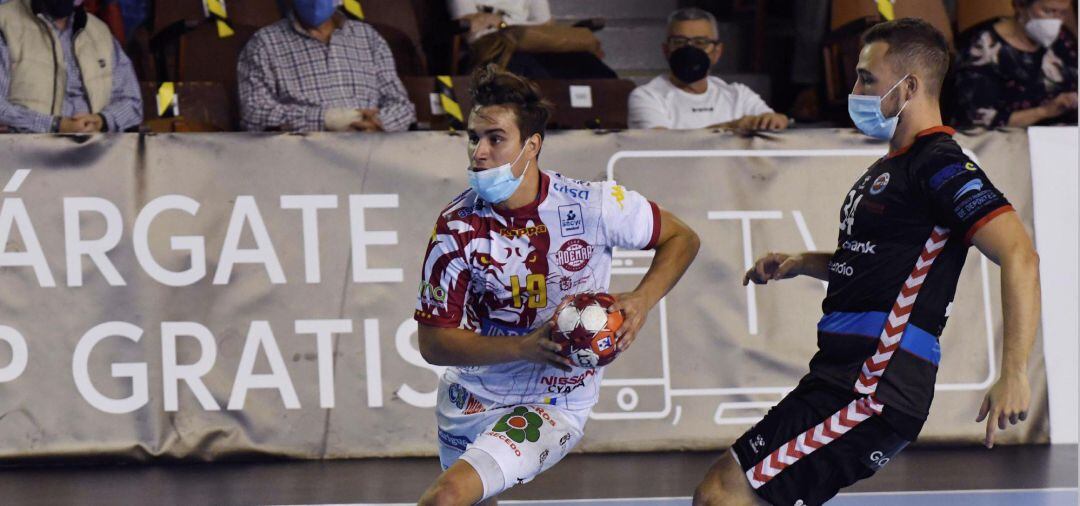 El jugador del Abanca Ademar Gonzalo Pérez (i) lanza ante la defensa del Sinfín Liberbank durante el partido de la octava jornada de la Liga Sacyr ASOBAL disputado hoy en el palacio municipal de deportes de León. Los jugadores de ambos equipos tuvieron que disputar el encuentro provistos de mascarilla debido a las medidas sanitarias impuestas por la Junta de Castilla y León para frena la expansión de la pandemia de la cpvid-19.