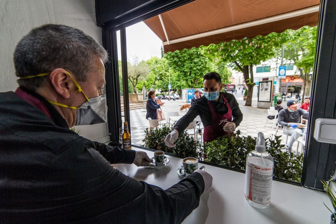 Un camarero coge varios cafés para servirlos en la terraza de un bar abierto en Cuenca