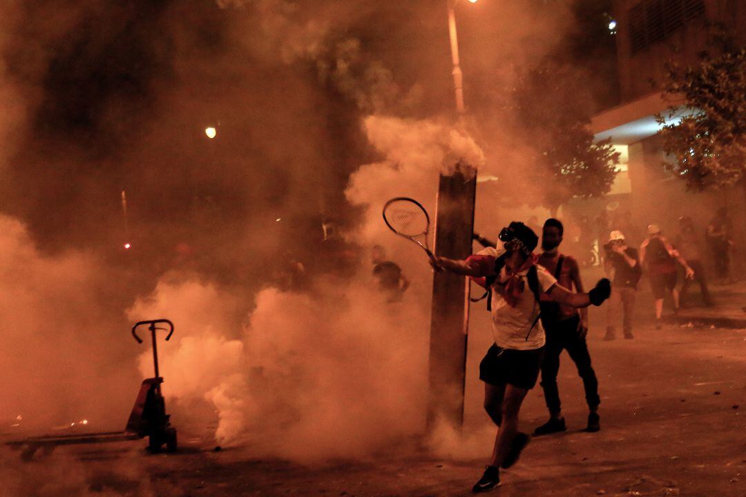 Un activista antigubernamental utiliza una raqueta de tenis para lanzar bombas lacrimógenas a la policía antidisturbios durante enfrentamientos cerca de la casa del Parlamento libanés