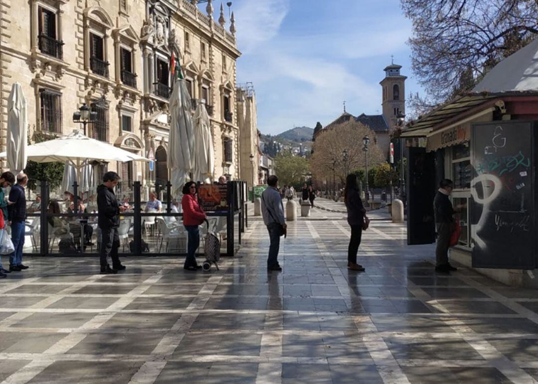 Las personas que la mañana del sábado 14 de marzo hacen cola para comprar en el kiosko de Plaza Nueva, en Granada, guardan la distancia de seguridad recomendada ante el avance del coronavirus