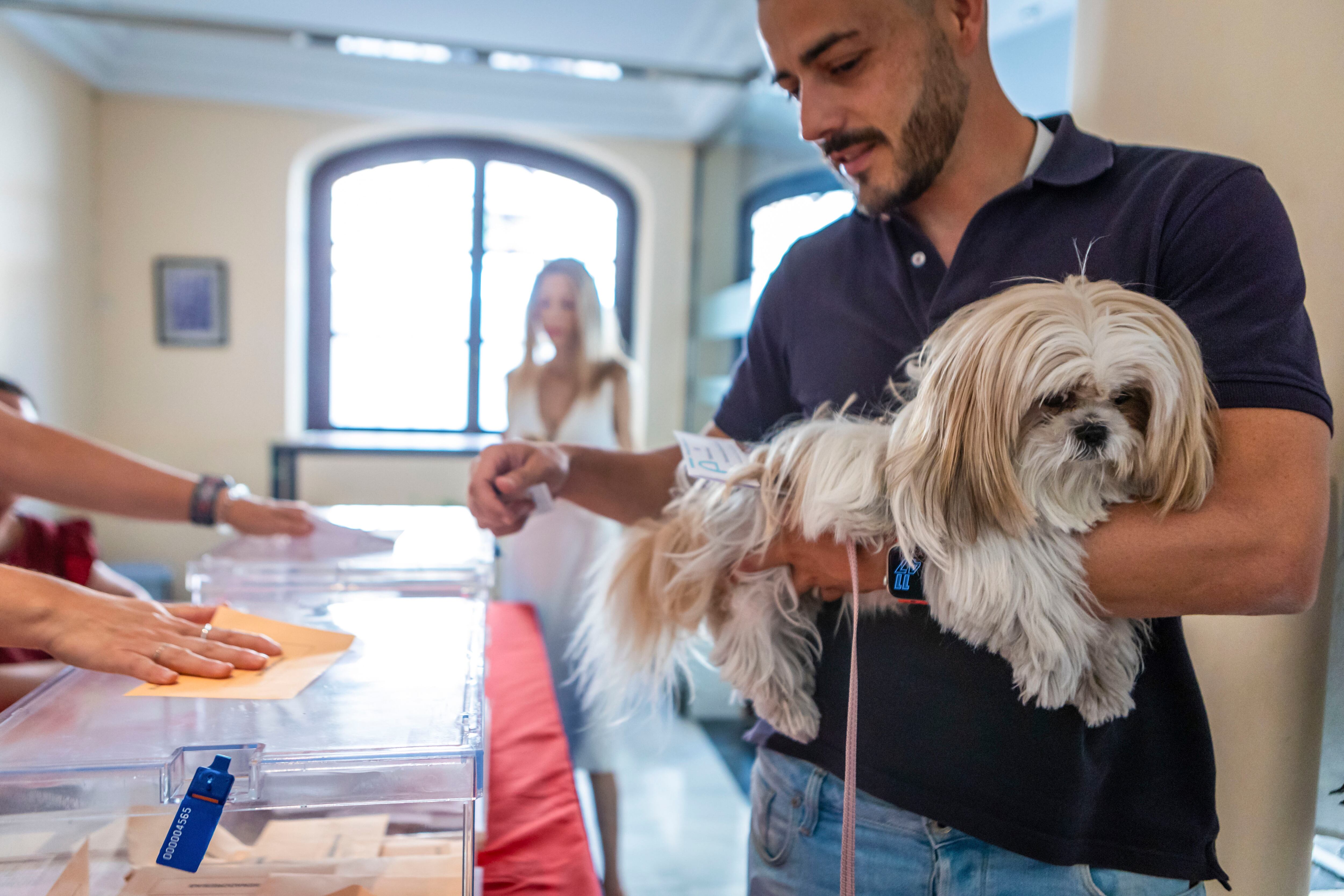 Un votante sostiene en brazos a su perro, mientras ejerce su derecho al voto en las elecciones generales de este domingo en el Ayuntamiento de Toledo 