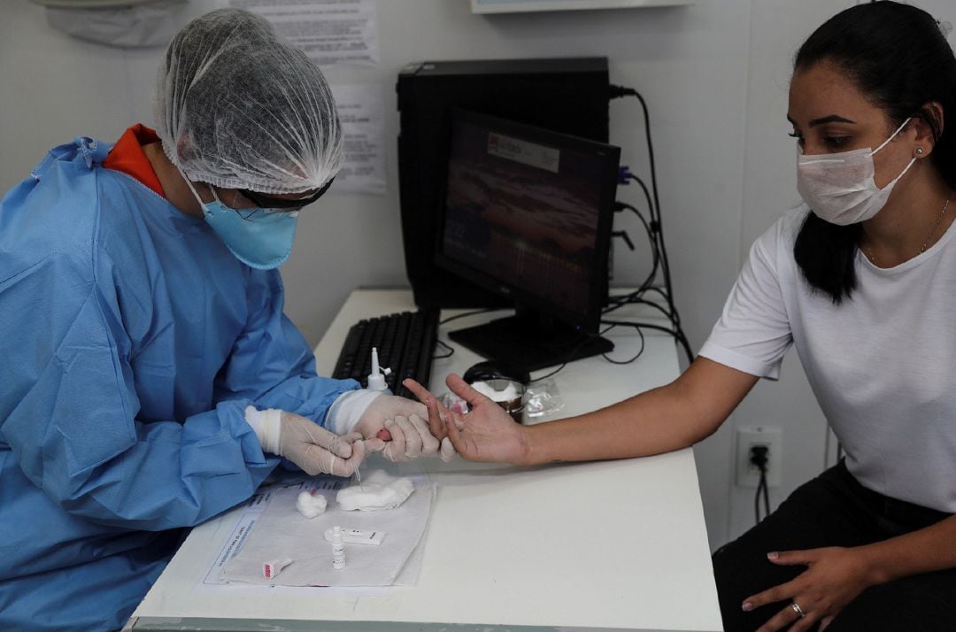 Fotografía de archivo fechada el 17 de abril de 2020 que muestra a Ariela Ramos (d), agente comunitaria de salud, mientras se somete a una prueba de coronavirus a través de muestras de sangre, este viernes, en Niterói, ciudad vecina a Río de Janeiro (Brasil)