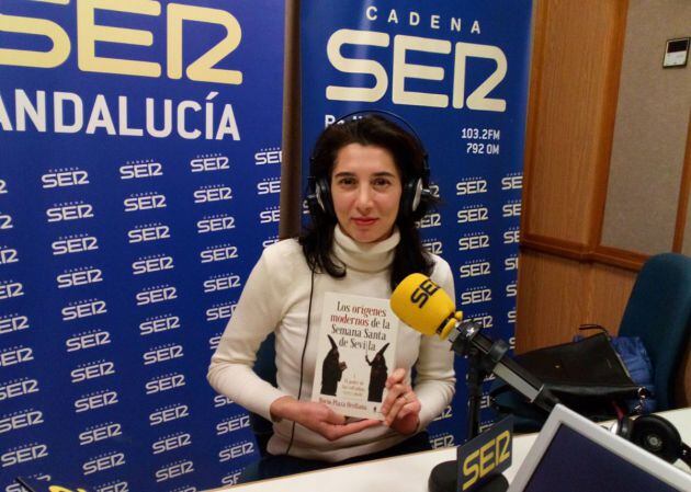 Rocío Plaza Orellana posa en el estudio de Cruz de Guía con un ejemplar de su libro 'Los orígenes modernos de la Semana Santa de Sevilla'