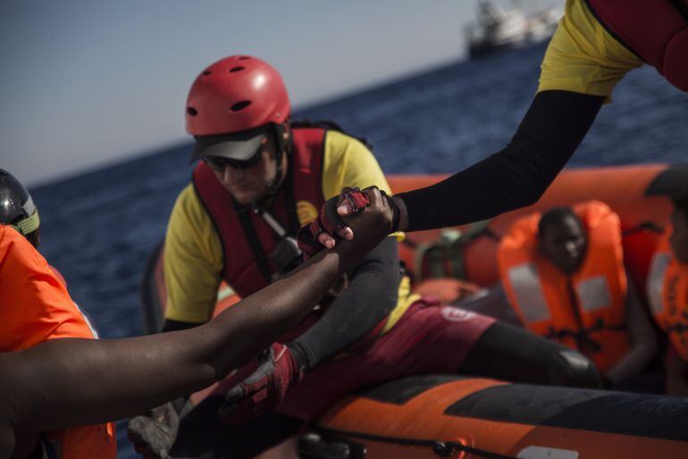 Un miembro de Proactiva Open Arms ayuda a un migrante a subirse a la embarcación de rescate.