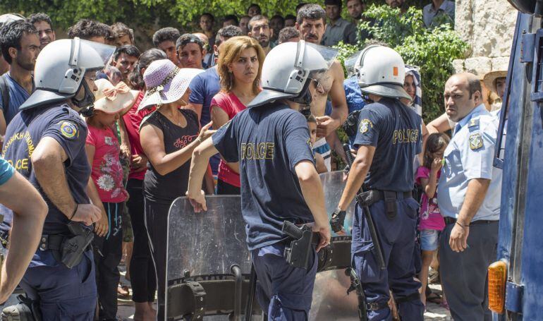 Varios policías vigilan a los inmigrantes que esperan en fila delante de la comisaría de la isla de Kos, Grecia.