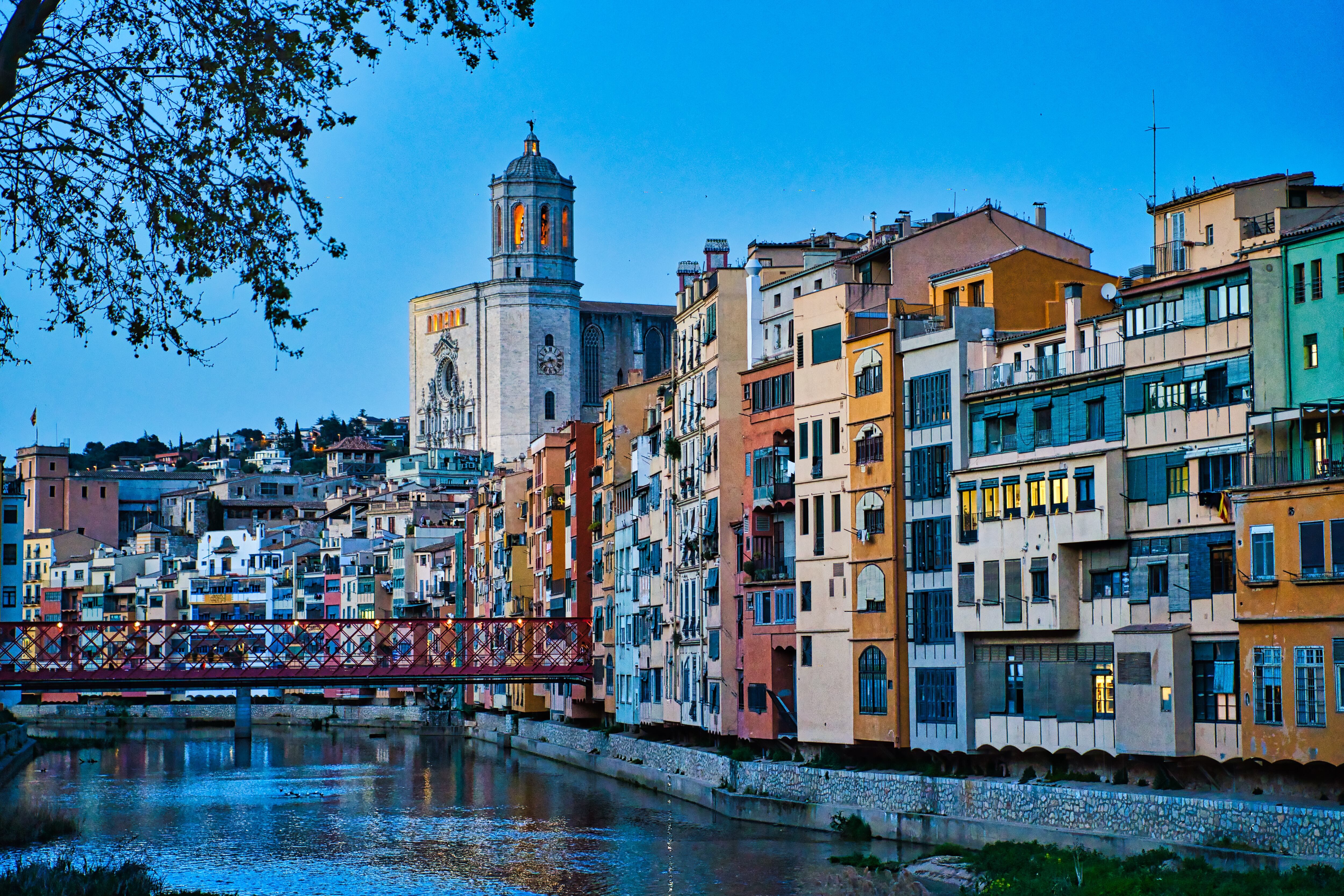 Hanging houses over the Onyar river in the historic center of Girona. All the river facades are painted in different colors. In the background the city&#039;s cathedral. Girona in March of 2021.