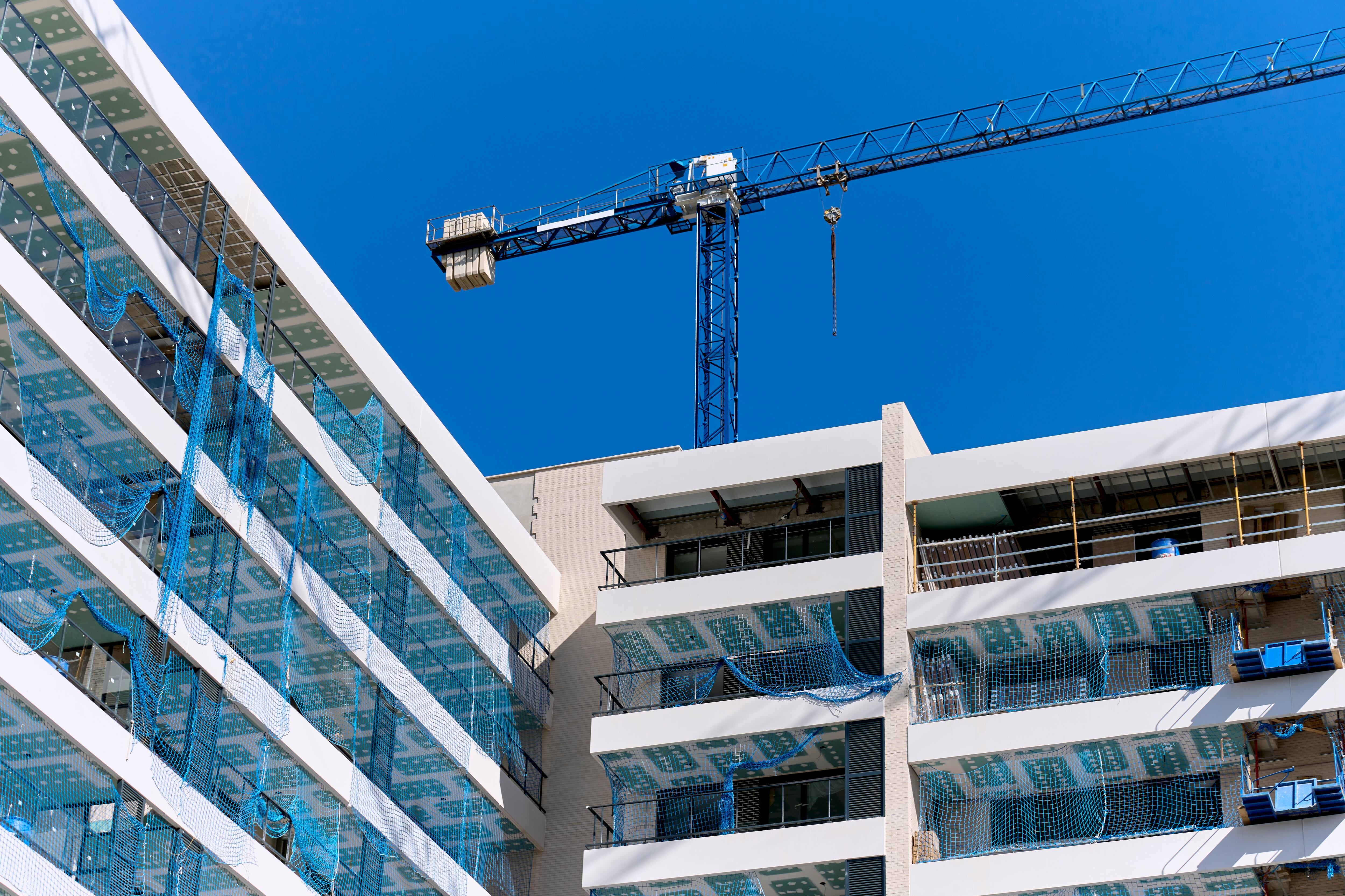 low angle view of a building under construction with a metal crane on the roof and a blue sky in the background.