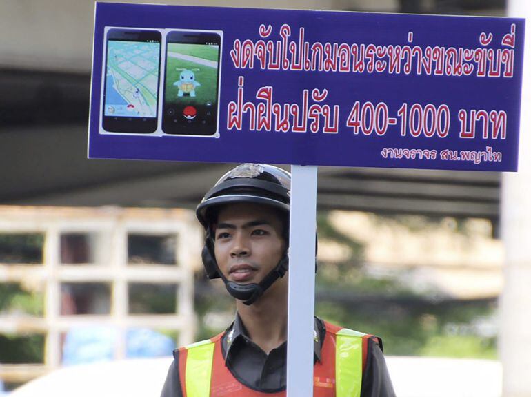 Un guardia de tráfico sostiene una pancarta en la que se lee &quot;No juege a Pokemon Go mientras conduce, los infractores serán multados&quot;.