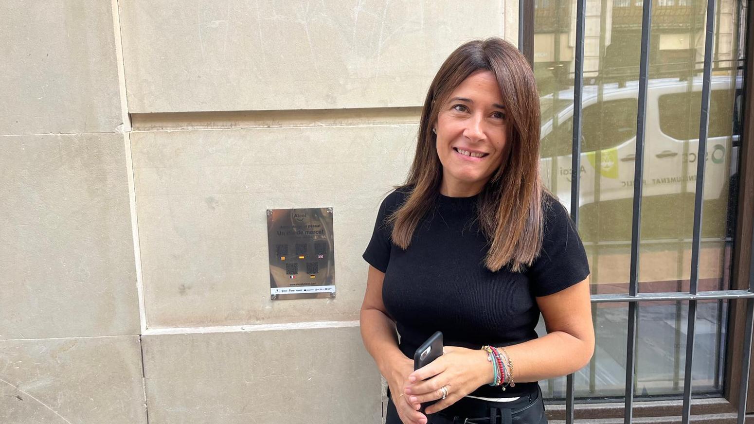 Lorena Zamorano, edil de Turismo, en el cartel con códigos QR situado en la calle San Lorenzo y que, a través del móvil, se puede ver la recreación de cómo era el mercado en la calle Pola Vieja (actual Sant Llorenç).