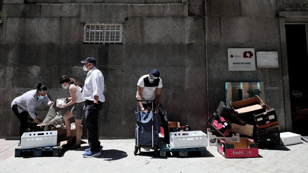 Dos personas recogen alimentos (izquierda y derecha) que les dan dos voluntarios a las puertas de la Parroquia Santa María Micaela en Madrid (España), a 29 de mayo de 2020.