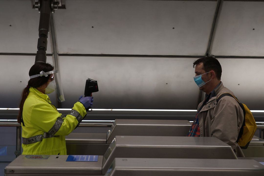 Una voluntaria de la DYA toma la temperatura con una pistola a un viajero en la estación de metro de Otxarkoaga