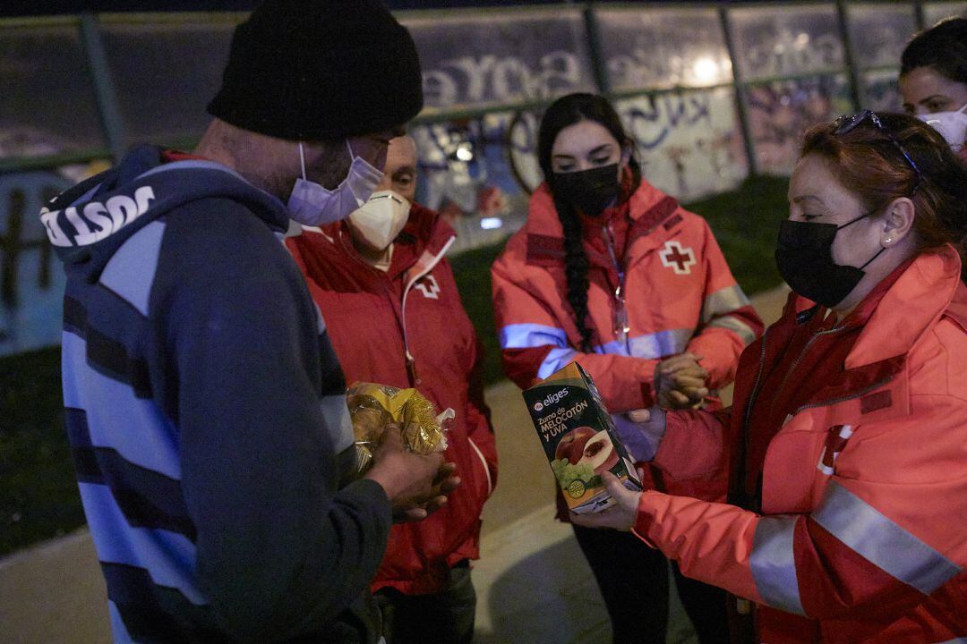 Varios trabajadores de Cruz Roja ofrecen comida a un hombre sin hogar