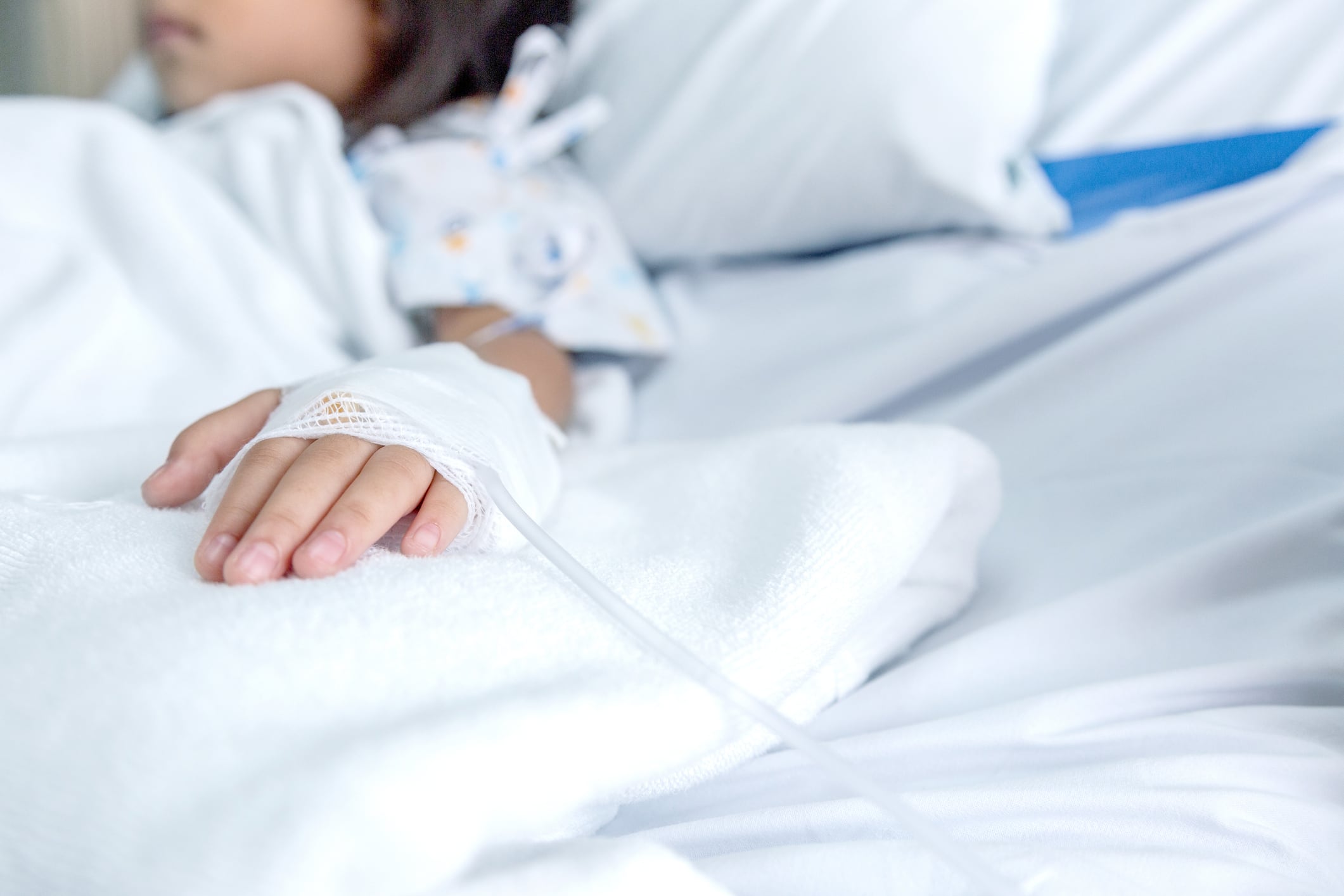 Niña en una cama de hospital, con la vía puesta en la mano