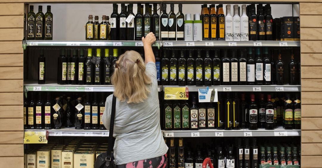 Una mujer coge una botella de aceite de una estantería del supermercado.