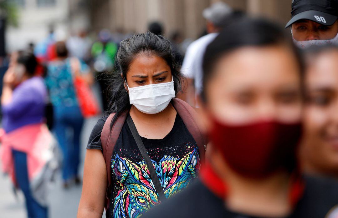 Una mujer con mascarilla camina entre la gente por la avenida del Zócalo en Ciudad de México.