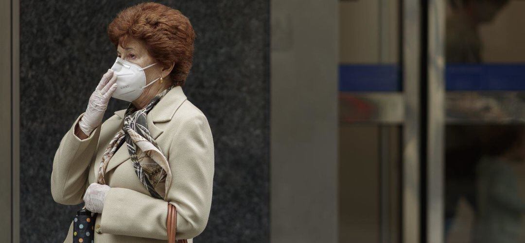 Una mujer pasea protegida contra el coronavirus con mascarilla FFP2 y guantes.