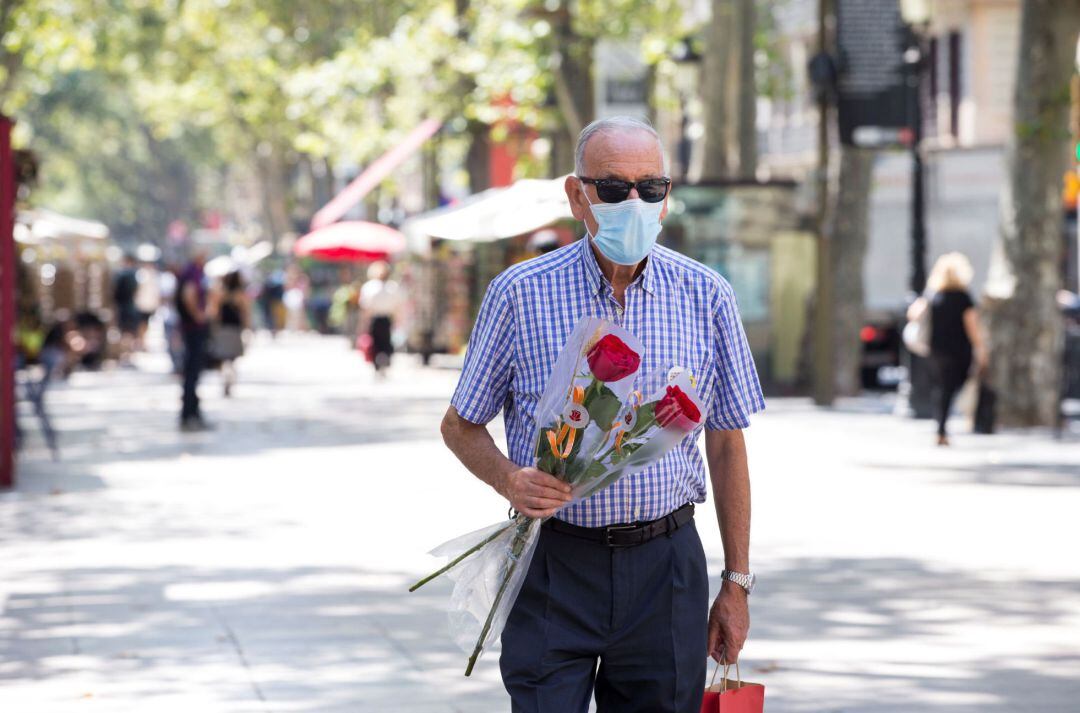 Un hombre con mascarilla porta un ramo de flores en el día de San Jordi en Barcelona.