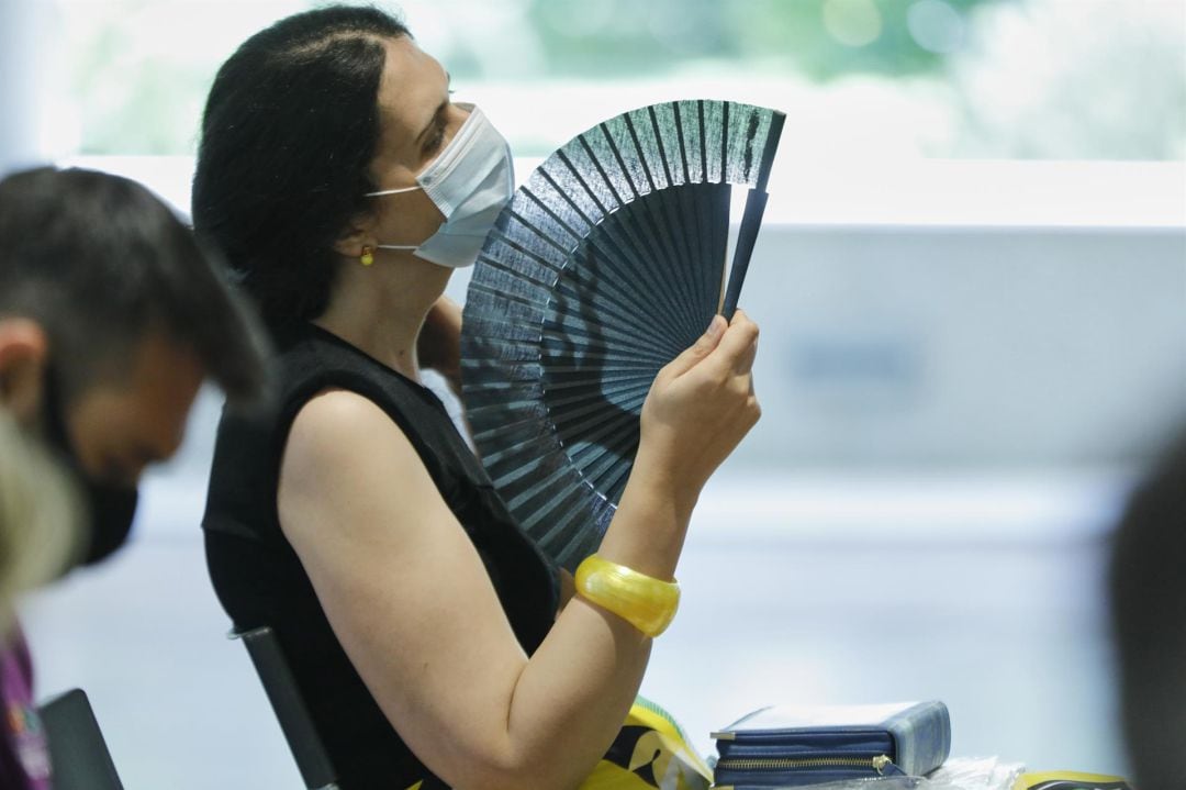 Una mujer con mascarilla se abanica