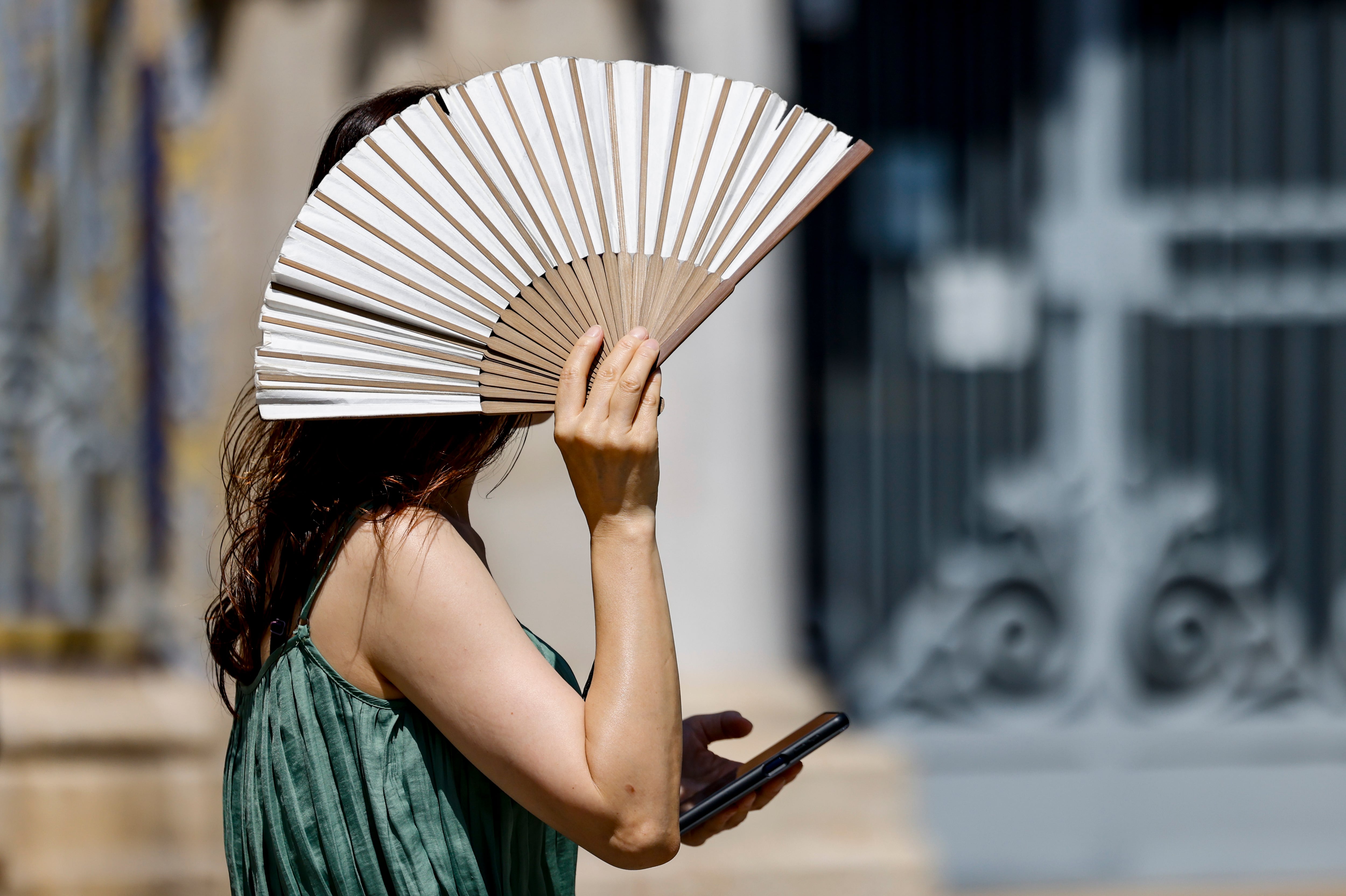 Una mujer se protege del sol con un abanico mientras pasea por la ciudad de València.