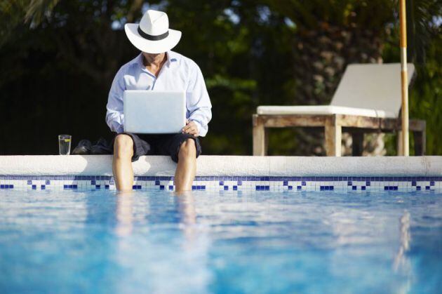 Hombre consultando un ordenador junto a la piscina.