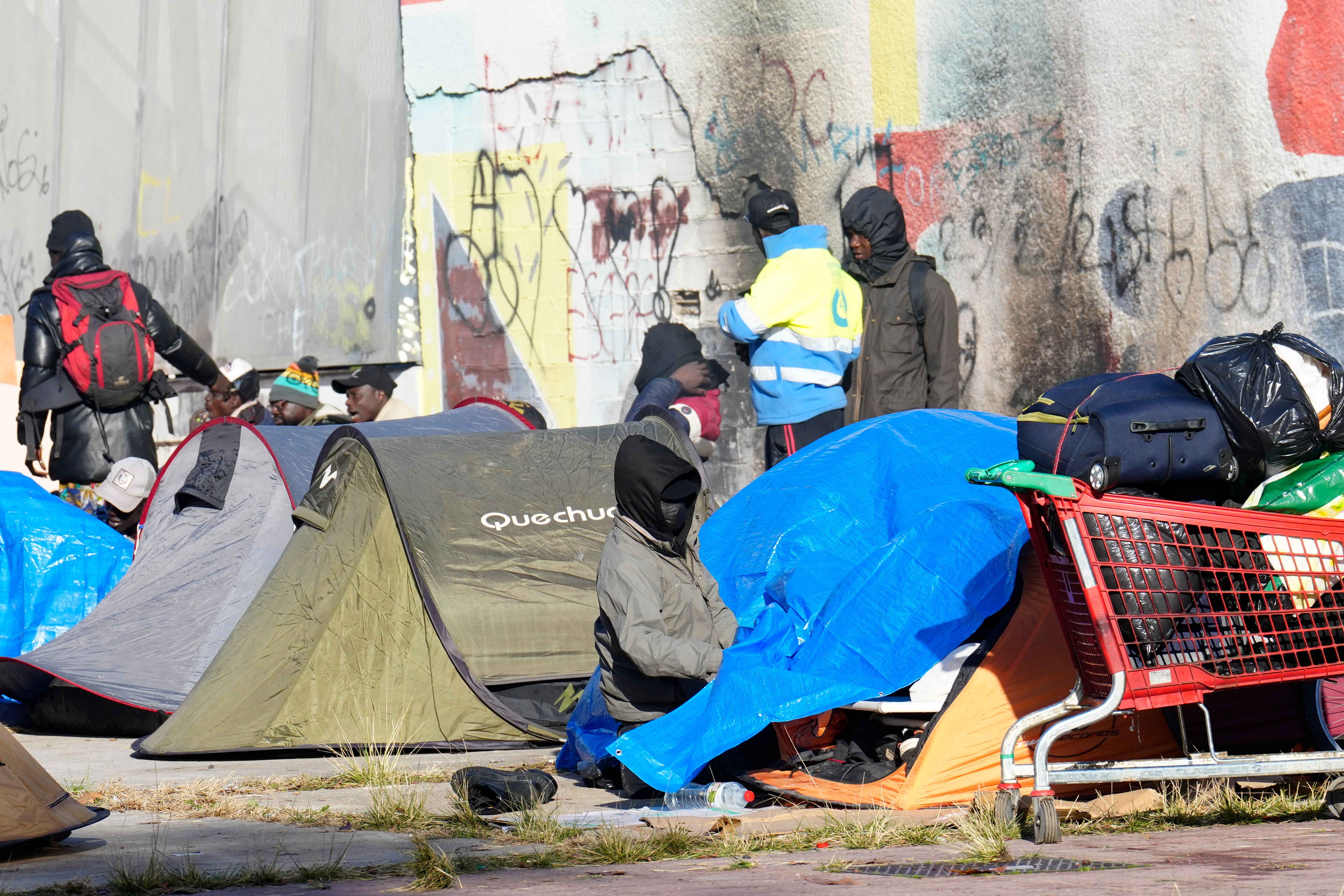GRAFCAT5902. BADALONA (BARCELONA) (ESPAÑA), 18/12/2025.- Aspecto este jueves del espacio donde el medio centenar de personas que fueron desalojadas ayer del antiguo instituto B9 de Badalona (Barcelona) han pasado la noche, una plaza que se encuentra delante del edificio desocupado, donde han instalado una decena de tiendas de campaña.EFE/ Alejandro García