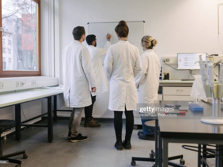 A group of medical students discussing some work while huddled around a whiteboard at the lab together.