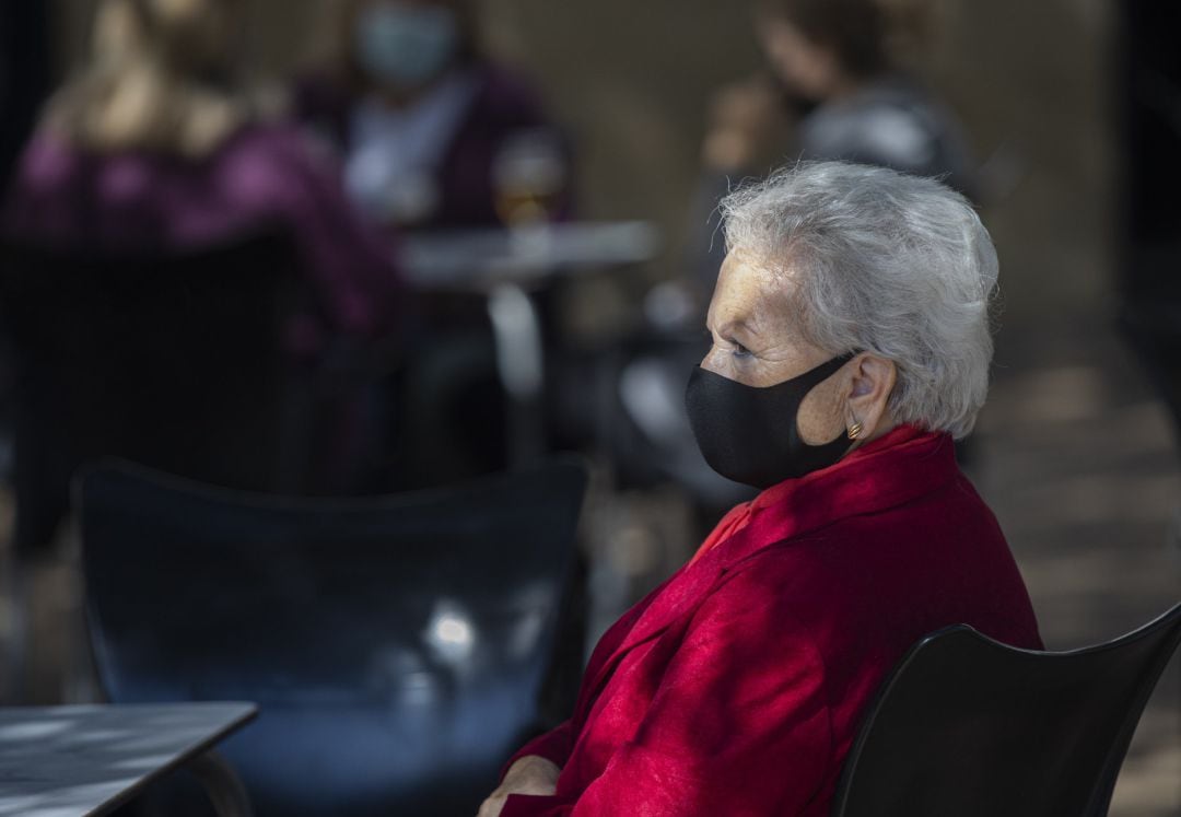 Una mujer mayor con mascarilla en la terraza de un bar.