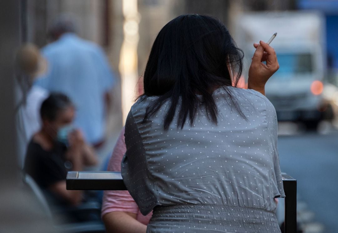 Una mujer fuma en una terraza. 