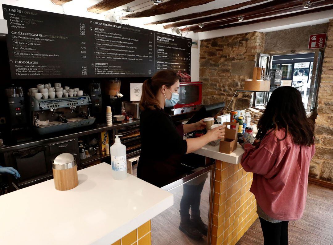 Interior de una cafetería en el centro de Pamplona donde una mujer compra dos cafés, en una jornada en la que Navarra vive su segundo día de confinamiento perimetral