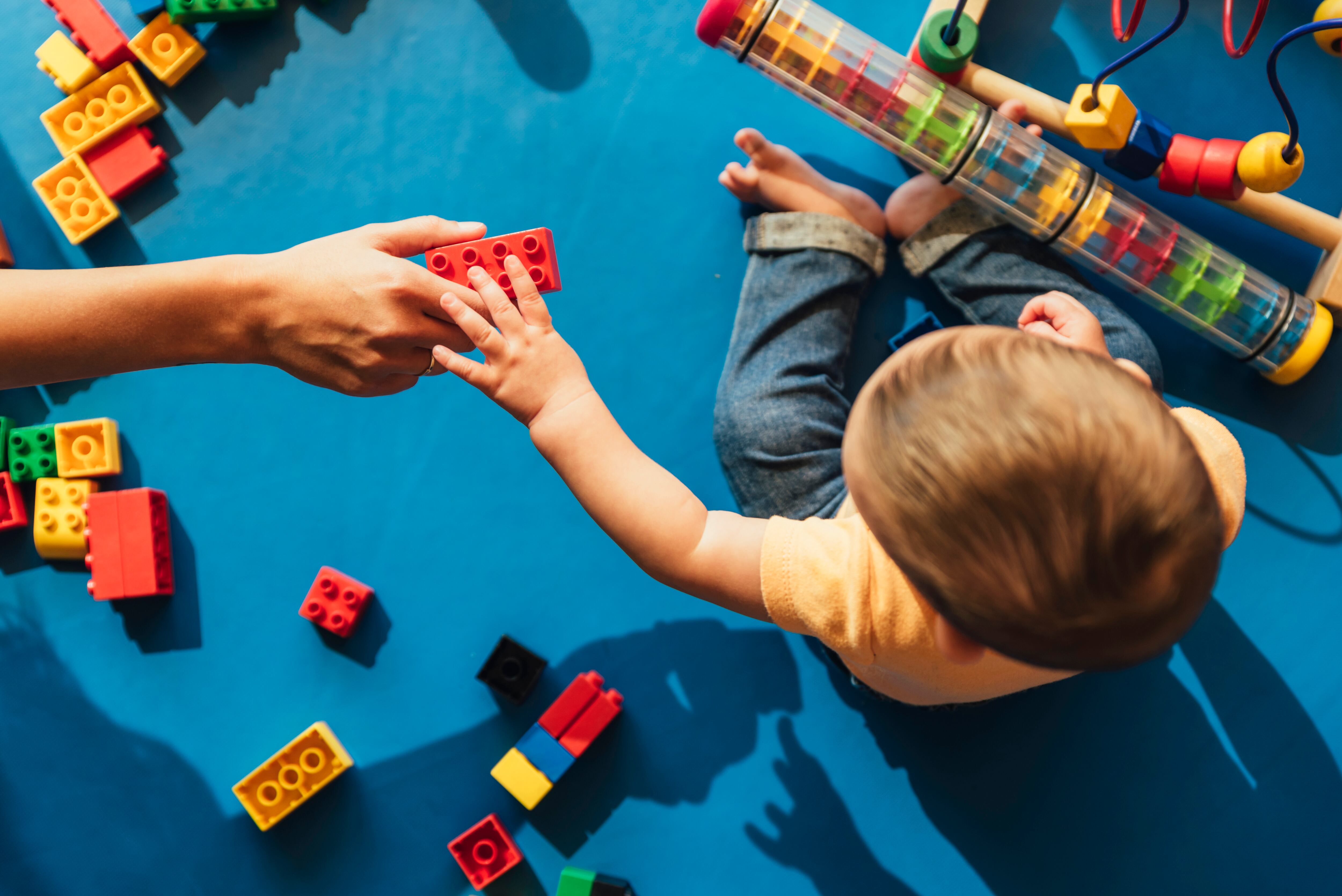 Happy baby playing with toy blocks in the kindergarten.