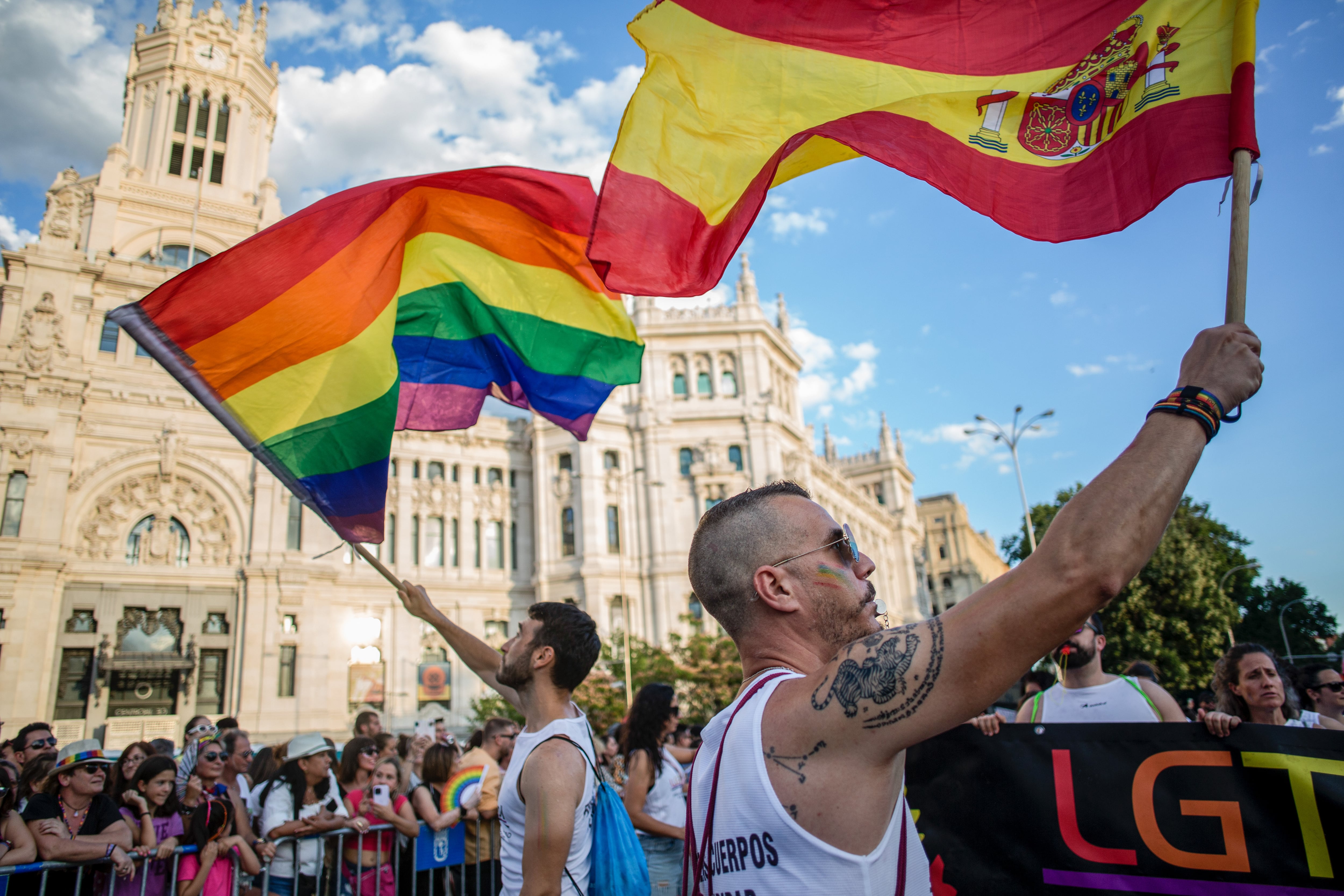 Dos hombres ondean la bandera LGTBI+ y la de España en el Orgullo de Madrid.