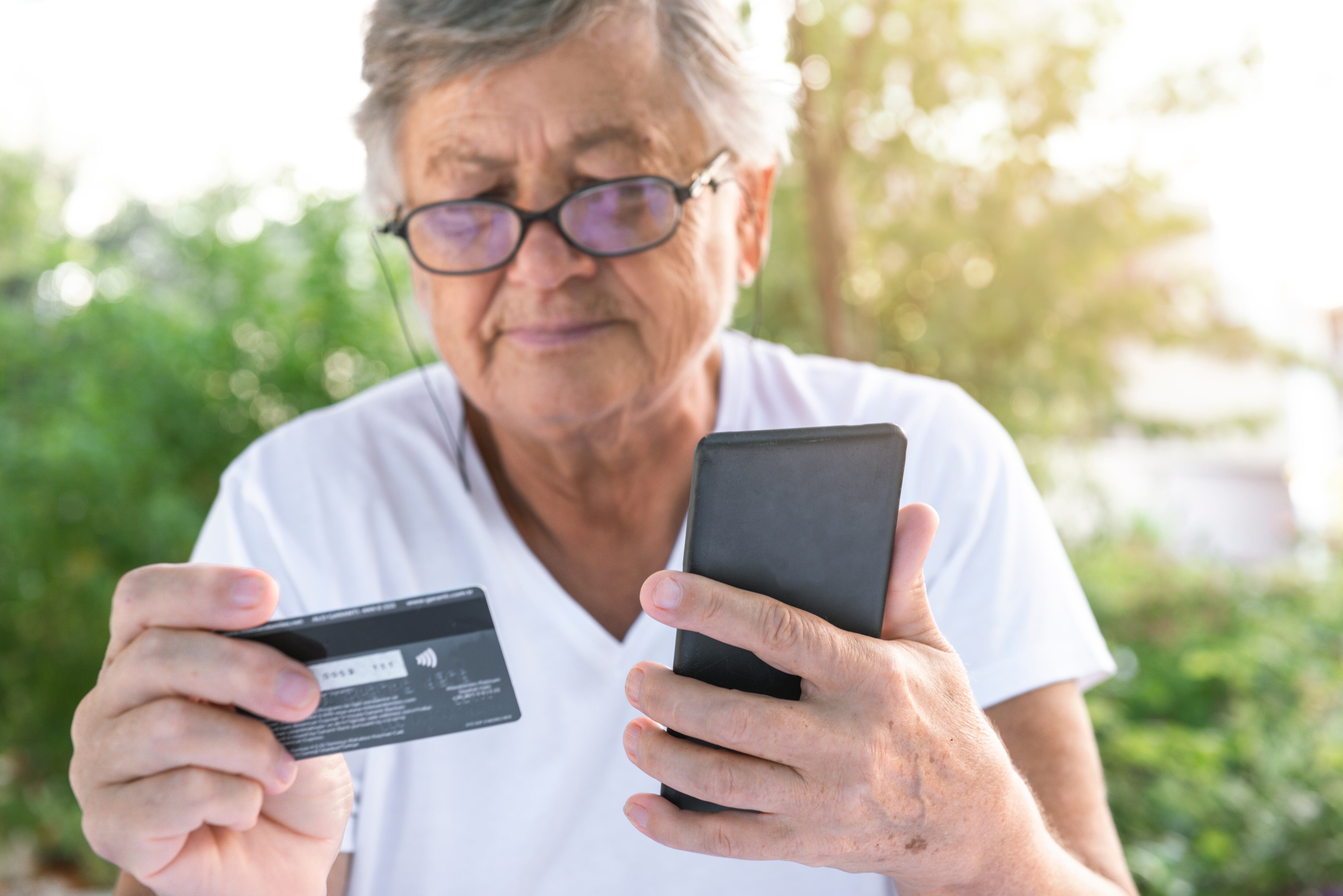 Senior woman using phone while holding credit card.