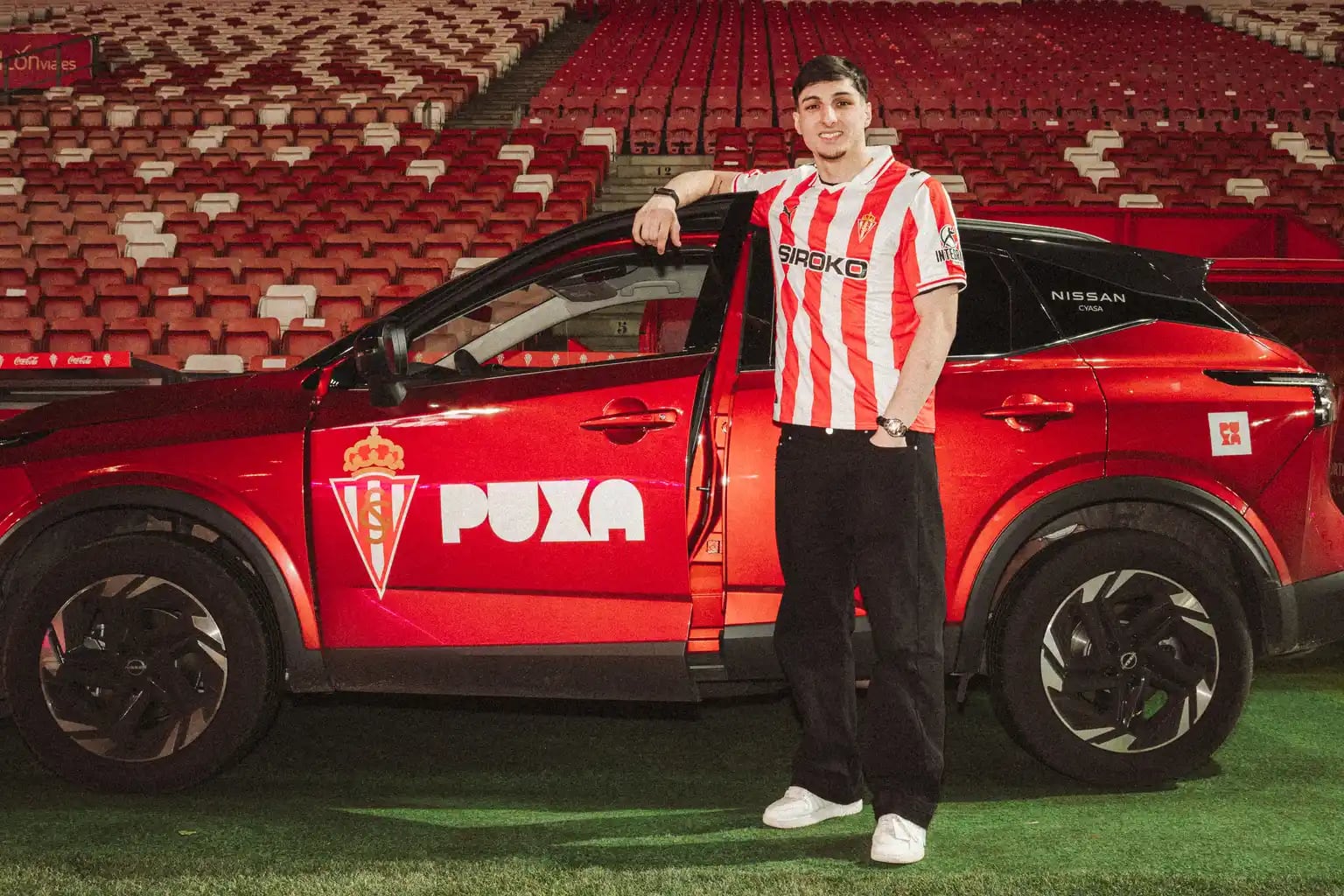 El delantero Andrés Ferrari posa junto a uno de los coches oficiales del Sporting.