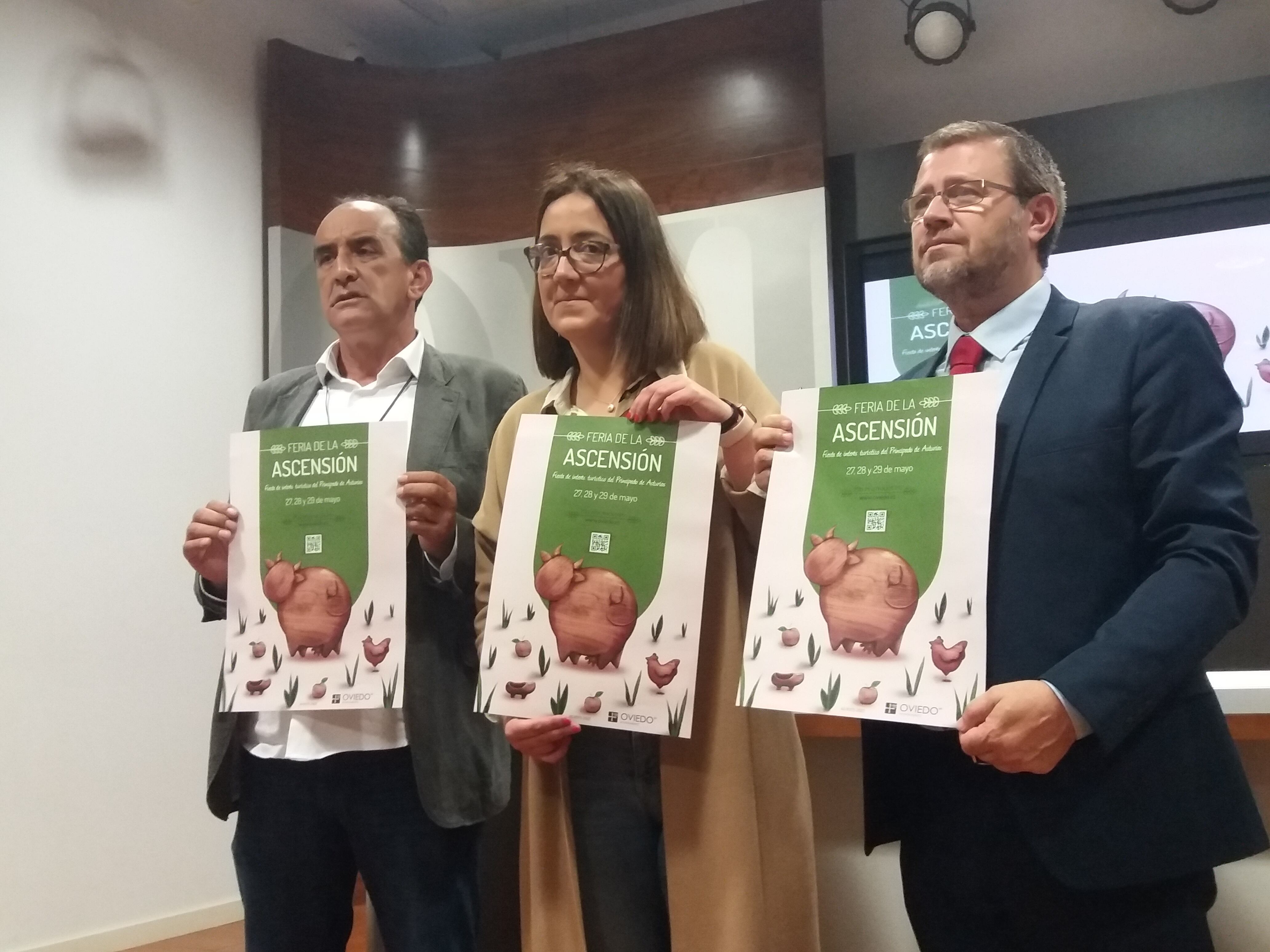 La concejala de Festejos de Oviedo, Covadonga Díaz, posa con el cartel de la Feria acompañada por el director técnico del concurso de ganados y un representante de Caja Rural de Asturias