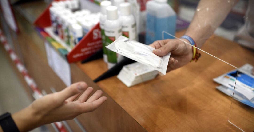 Un farmacéutico entrega a un cliente una de las mascarillas KN95 que ha recibido en la farmacia Tucán.