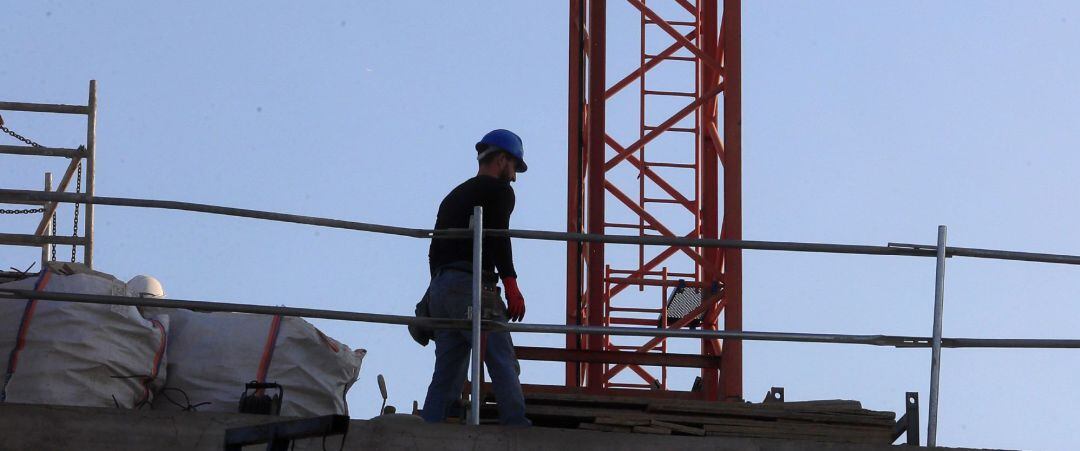 Un obrero permanece junto a una grúa de construcción