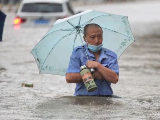 Una persona con un paraguas avanza por la calle con medio cuerpo sumergido en el agua.