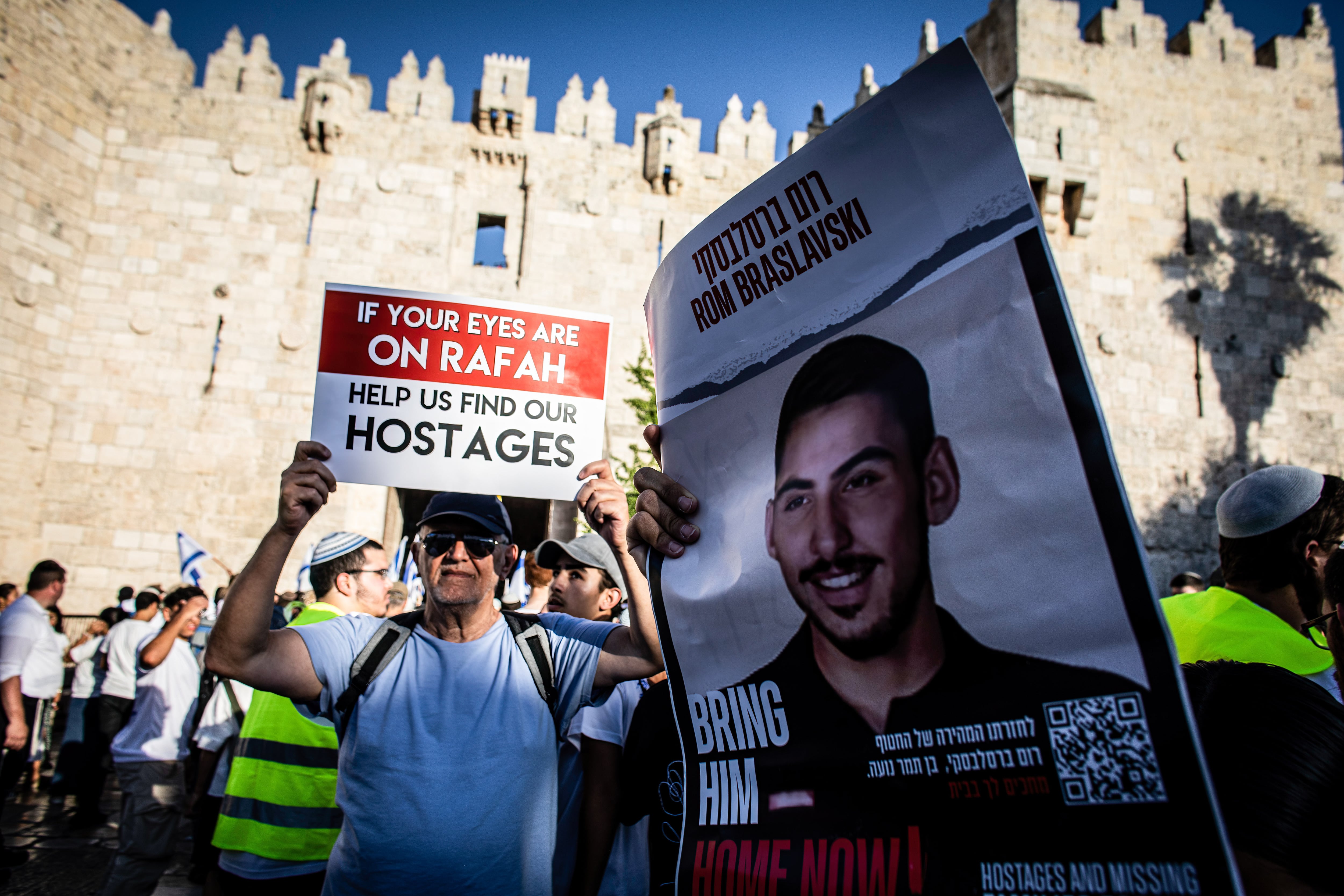Un hombre sostiene un cartel junto a un cartel que muestra una foto de Rom Braslavsky
