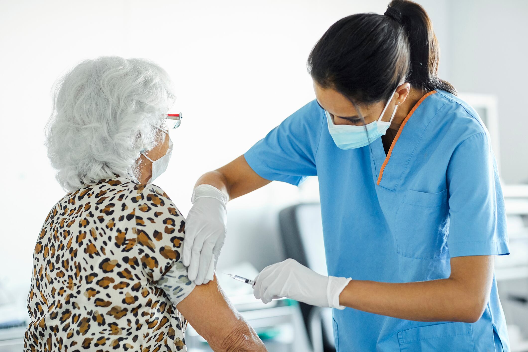 Nurse injecting syringe on arm of elderly patient. Female medical professional is working at hospital. They are in clinic during COVID-19.